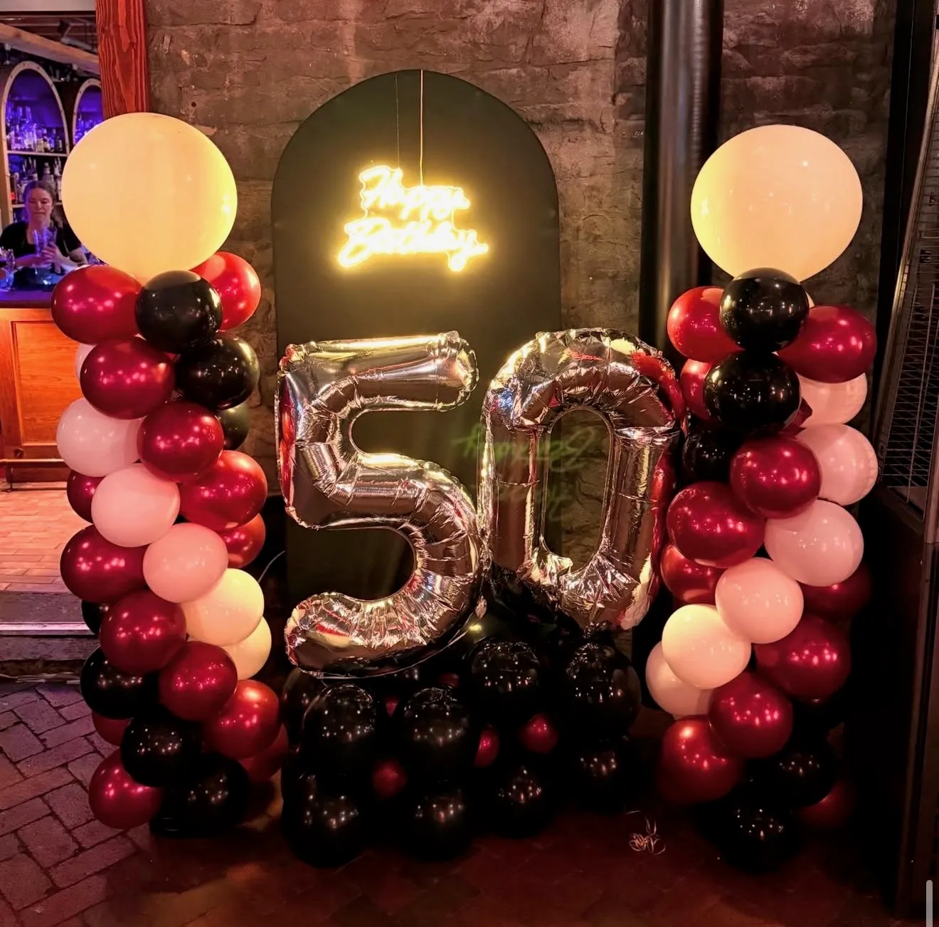 Burgundy, black and cream balloon columns topped with oversized pearl balloons beside a silver 50 number balloon.